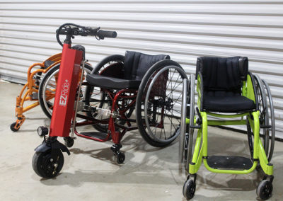 An image of three WCMX rigid frame wheelchairs - burnt orange, red, and lime green. The red wheelchair has the EZRide unit connected